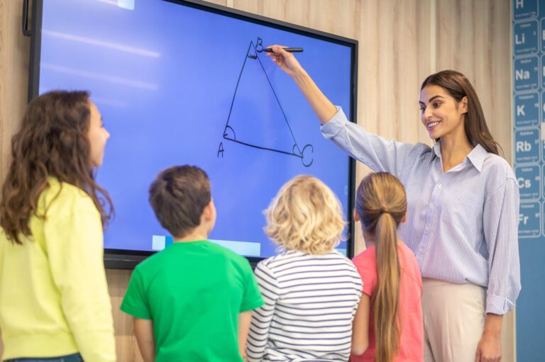 معلم به دانش‌آموزان با استفاده تخته هوشمند آموزش می‌دهد