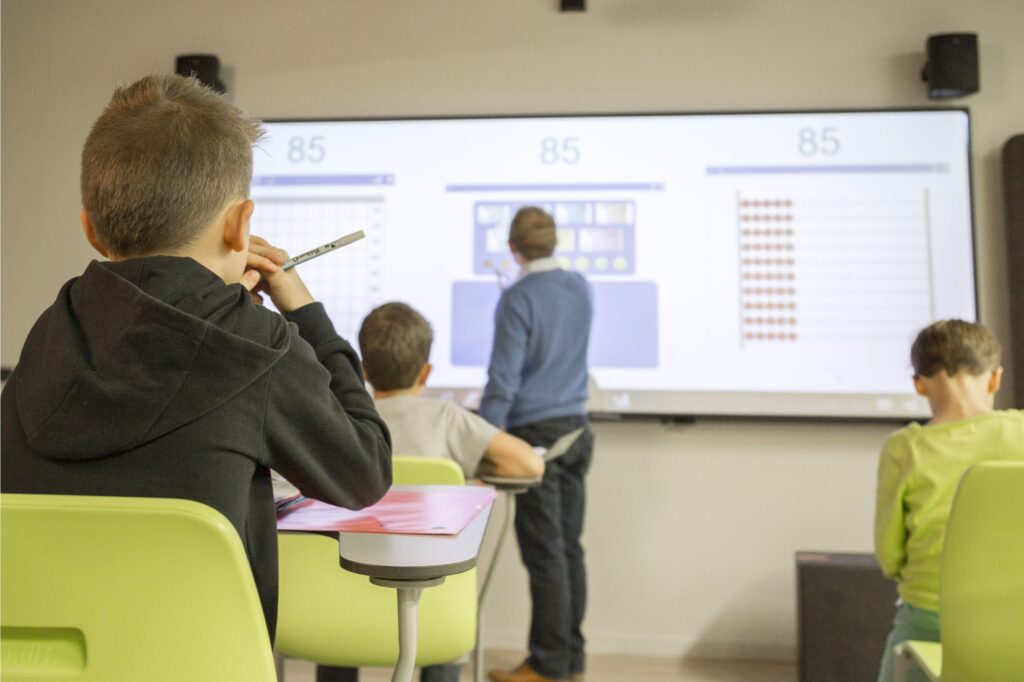 معلم در حال تدریس روی تخته هوشمند و توجه دانش‌آموزان